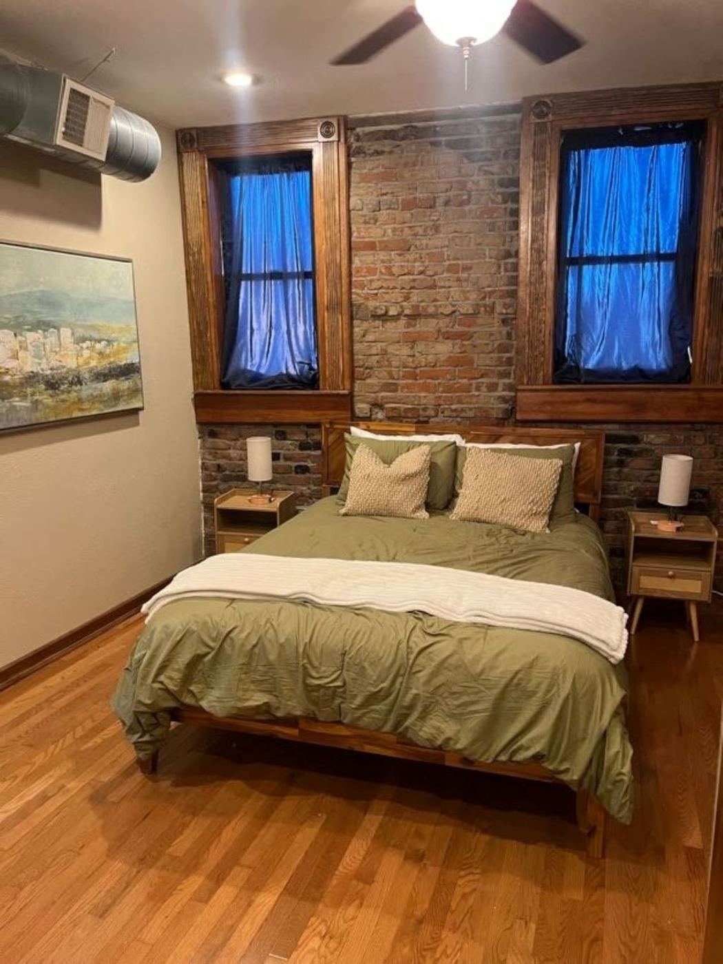 Bedroom with olive green bedding, brick wall, and two tall windows